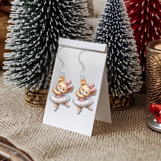 Christmas-themed table setting with decorative trees, candles, and a card with earrings on a burlap surface.
