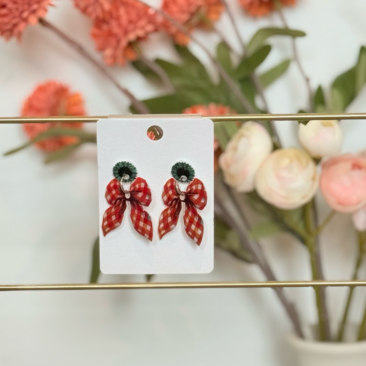 Red bow-shaped earrings on a card with a blurred floral background