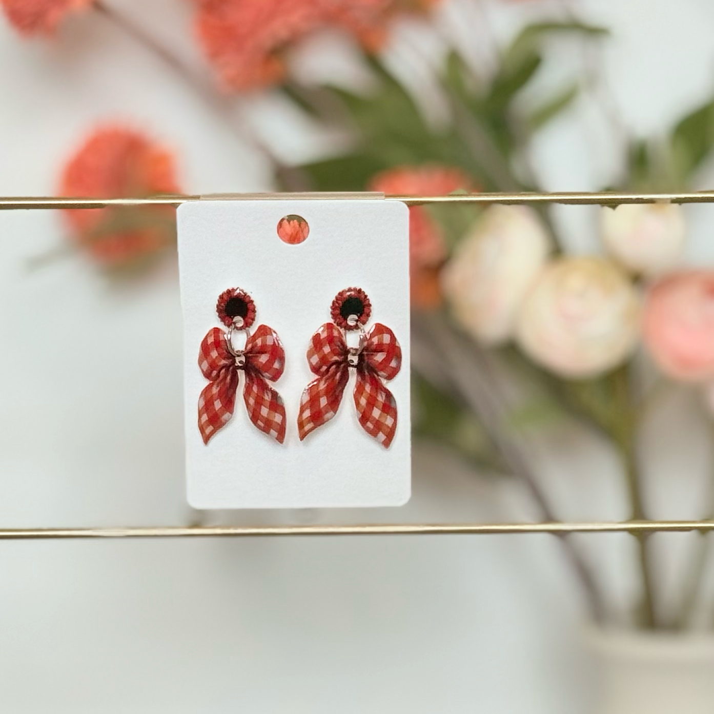Pair of red butterfly earrings on a white card with a blurred floral background